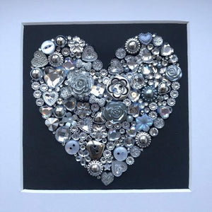 silver sparkly heart button art on black background. Framed picture.